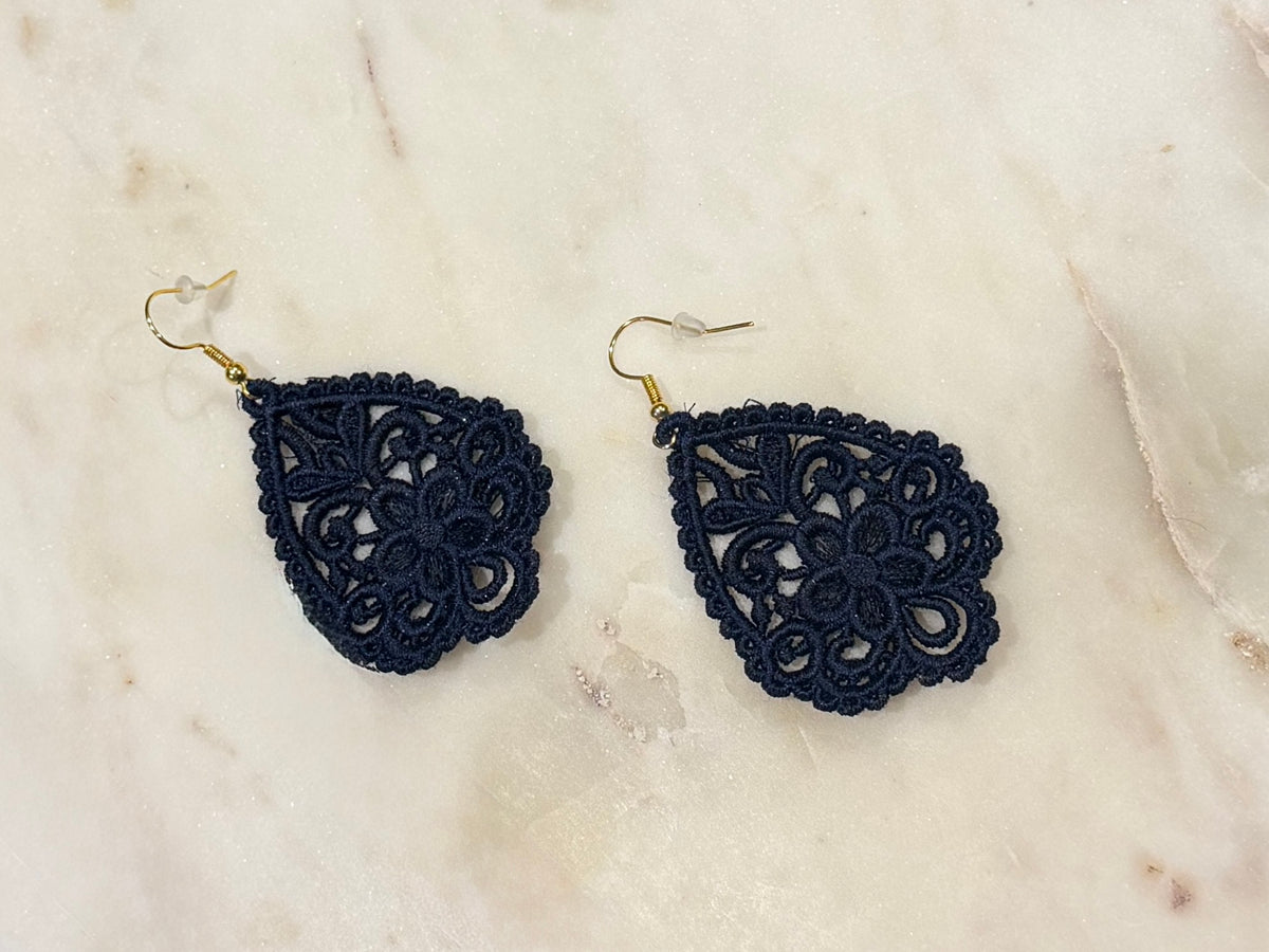 A pair of navy blue embroidered ace drop earrings with gold fishhook wires, displayed on a light beige marble surface.