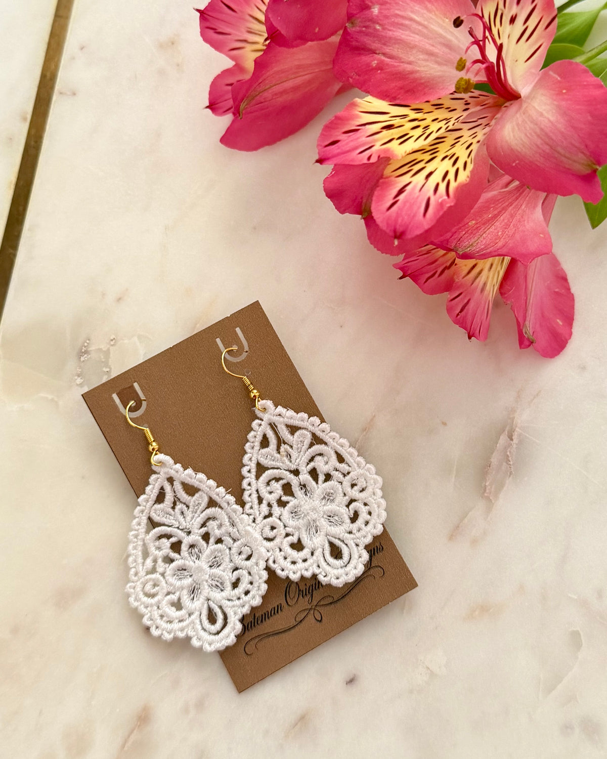 White and gold teardrop earrings made from embroidery on display card